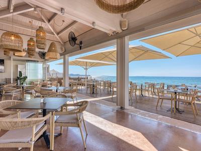 Offener Hotelrestaurantbereich mit Rattanmöbeln und Blick auf Terrasse und Meer.