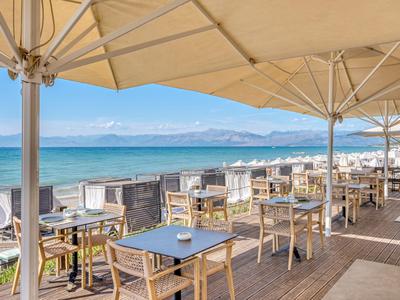 Blick auf eine offene Terrasse mit Holzmöbeln und Sonnenschirmen am Meer.