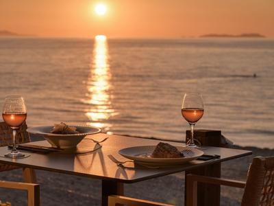 Zwei Gläser Wein und Essen auf einem Tisch mit Blick auf einen Sonnenuntergang am Meer.