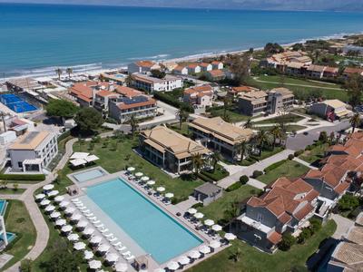 Blick auf ein Hotelresort mit Pools, Sonnenschirmen und Gebäuden am Meer.