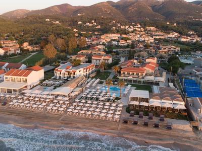 Strandhotel mit Sonnenliegen und Hütten am Meer, umgeben von Bergen und Siedlungen.