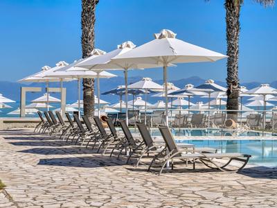 Poolbereich mit Liegestühlen und Sonnenschirmen an einem Hotel mit Meerblick.