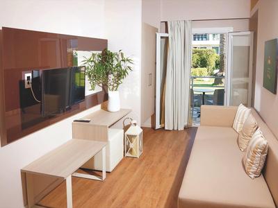 Moderner, heller Wohnraum mit Holzfußboden, beiger Couch, großem Fernseher und Pflanzen nahe Fenster.