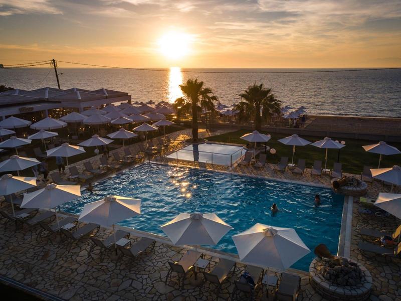 Sonnenuntergang über einem Pool mit Sonnenschirmen und Palmen am Strand.