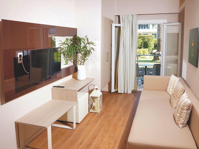 Modern eingerichtetes Wohnzimmer mit Sofa, TV, Pflanzen und großem Fenster mit Blick ins Grüne.