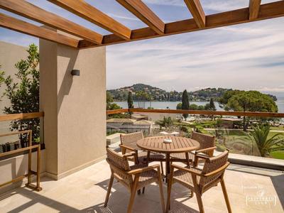Balkon mit Holztisch und vier Stühlen mit Blick auf See und bewaldete Hügel.