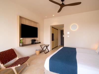 Modernes Hotelzimmer mit großem Bett, Wand-TV, Sessel und Deckenventilator.