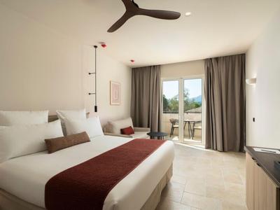 Modernes Hotelzimmer mit großem Bett, Ventilator und Zugang zu Balkon mit Sitzgelegenheit.