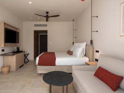 Modern eingerichtetes Hotelzimmer mit Bett, Sofa und Fernseher in neutralen Farben.