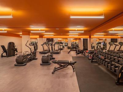 Gut ausgestatteter Fitnessraum mit verschiedenen Trainingsgeräten und Hanteln in warm beleuchtetem Raum.