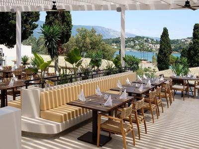 Terrasse eines Hotels mit Holztischen, Stühlen und Blick auf die Küstenlandschaft.