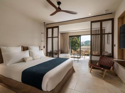 Modernes Hotelzimmer mit großem Bett, Holzstuhl und Blick auf Terrasse und Landschaft.