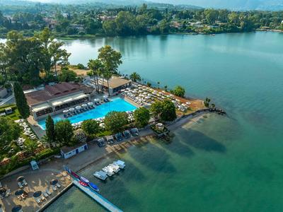 Hotel mit großem Swimmingpool und Terrasse am Ufer eines klaren Sees, umgeben von grüner Natur.