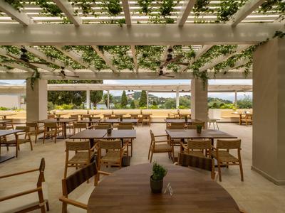 Offener Outdoor-Bereich eines Hotels mit Holzmöbeln und Blick auf das Meer.