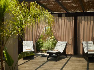 Überdachte Terrasse mit Holzlatten als Dach, zwei Liegestühle und Klapptisch, Pflanzen im Hintergrund.
