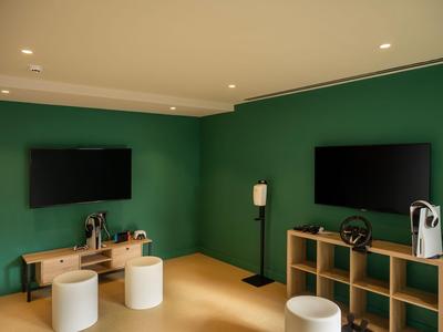 Moderner Hotelzimmerbereich mit grün gestrichener Wand, zwei Fernsehern und minimalistischen Möbeln.