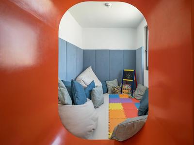 Blick durch einen orangefarbenen Bogen in einen gemütlichen Raum mit Kissen und bunten Spielmatten.