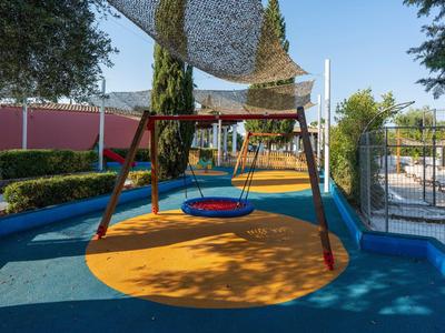 Schaukelplatz mit blauem und gelbem Gummiboden in einer entspannenden Außenhotelumgebung.