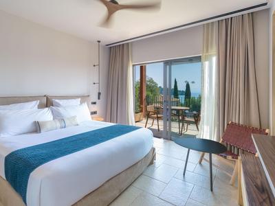Modernes Hotelzimmer mit großem Bett, Balkon und Blick auf eine sonnige Terrasse.
