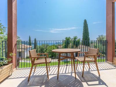 Ein Balkon mit zwei Stühlen und einem Tisch, Blick auf grüne Bäume und blauen Himmel.