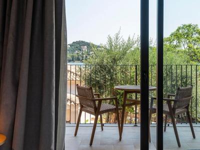 Balkon mit Stühlen und Tisch, Blick auf grüne Bäume und Hügel im Hintergrund.