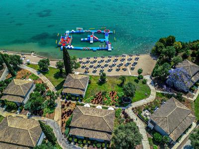 Luftaufnahme eines Strandresorts mit Sonnenschirmen, Wasserspielplatz und mehreren Gebäuden.