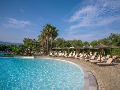 Großer Hotelpool mit Liegestühlen und Sonnenschirmen an einem sonnigen Tag.