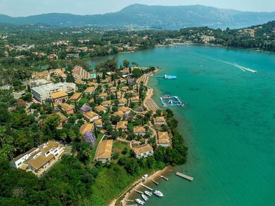 Luftaufnahme eines Resorts mit Gebäuden am Ufer eines türkisfarbenen Meeres und umliegenden Bergen.