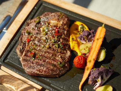 Gegrilltes Steak mit Kräutern, begleitet von Gemüse auf schwarzem Steinservierbrett.
