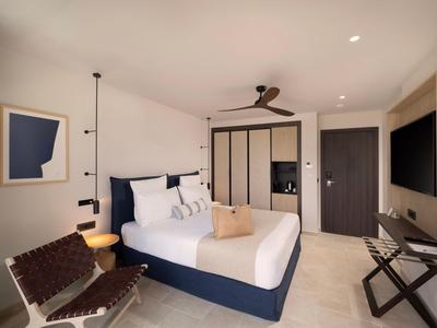 Modernes Hotelzimmer mit großem Bett, Wandleuchte, Stuhl und Deckenventilator.
