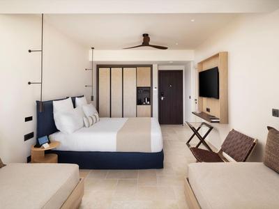 Modernes Hotelzimmer mit Doppelbett, TV, Sitzbereich und Kleiderschrank in neutralen Farben.