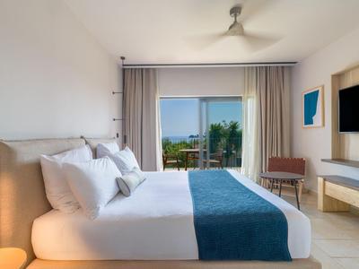 Modernes Hotelzimmer mit großem Doppelbett, weißer Bettwäsche und blauem Bettläufer, Blick auf Terrasse.