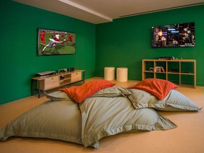 Gemütlicher Sitzbereich mit Kissen, grün lackierten Wänden und zwei hängenden Fernsehern im Hotelzimmer.