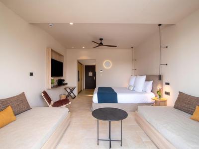 Modernes Hotelzimmer mit zwei Sofas, Bett und minimalistischer Einrichtung in neutralen Farben.