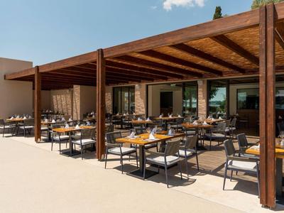 Offener Essbereich mit Holzdach, Tischen und Stühlen eines Hotels bei sonnigem Wetter.