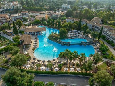 Großer Hotelpool mit Inselbar, umgeben von Liegestühlen und grüner Vegetation.