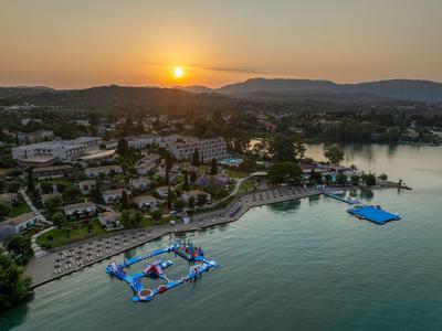 Sonnenuntergang über einem See mit einem Hotelresort und schwimmenden Wasserattraktionen.
