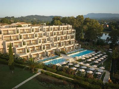 Moderner Hotelkomplex mit Pools, Liegestühlen und Blick auf grüne Landschaften bei Sonnenuntergang.