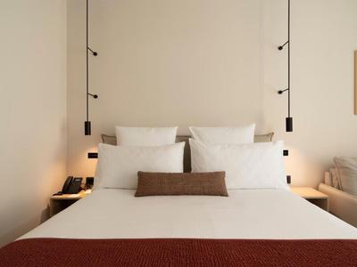 Schlichtes, modern eingerichtetes Hotelbett mit weißen Kissen und braunem Akzentkissen.