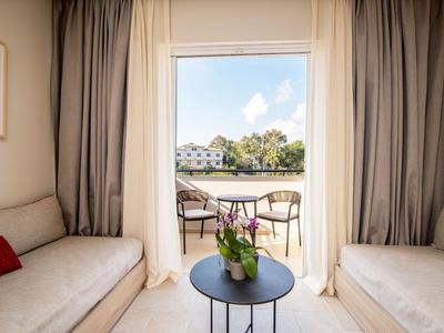 Helles Hotelzimmer mit zwei Sofas und Blick auf Terrasse und Wasser.