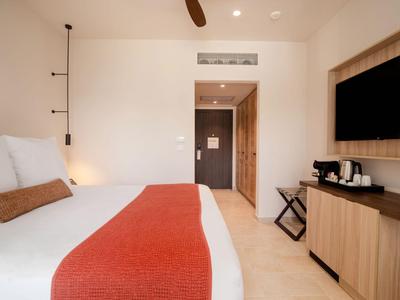 Modernes Hotelzimmer mit großem Bett, roter Bettdecke und TV an der Wand.