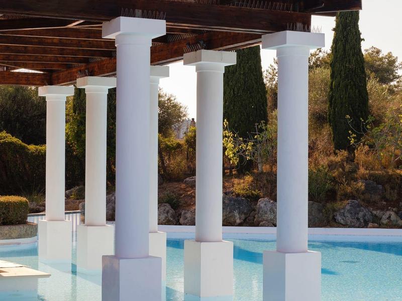 Weiß gestrichene Säulen tragen ein Holzpergola über klarem Wasser mit Umgebung aus Bäumen und Garten.