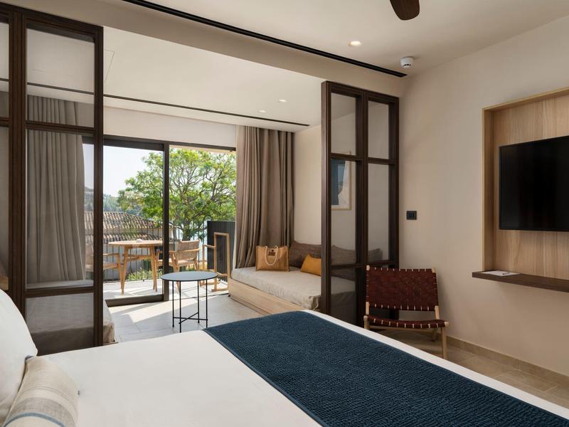 Modernes Schlafzimmer mit großem Bett, Glas-Schiebetüren, Balkon und Sitzbereich in neutralen Farben.