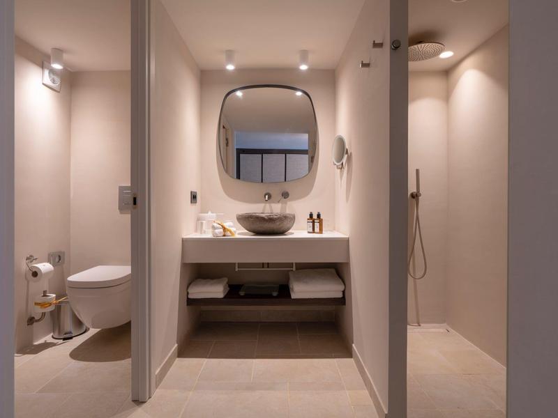 Modernes Badezimmer mit weißen Wänden, runder Spiegel, Waschbecken, Toilette und begehbarer Dusche.