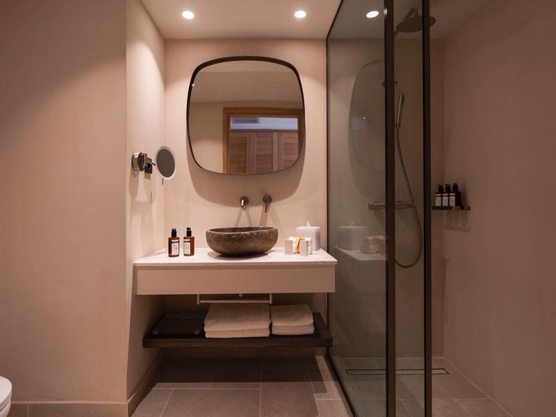 Moderner Badezimmerschrank mit rundem Spiegel, Waschbecken, Beleuchtung und Glasscheibendusche.