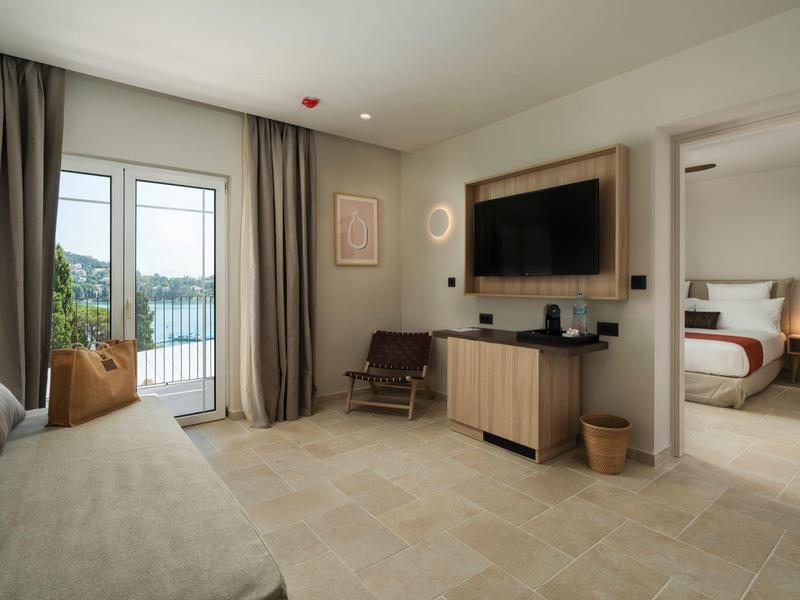 Helles Wohnzimmer mit Couch, Fernseher an der Wand und Blick in ein angrenzendes Schlafzimmer.