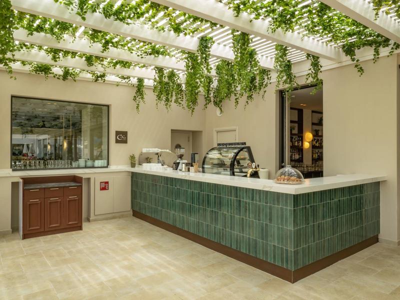 Moderner Verkaufsstand mit grün gefliester Theke, Glasvitrinen und hängenden grünen Pflanzen.