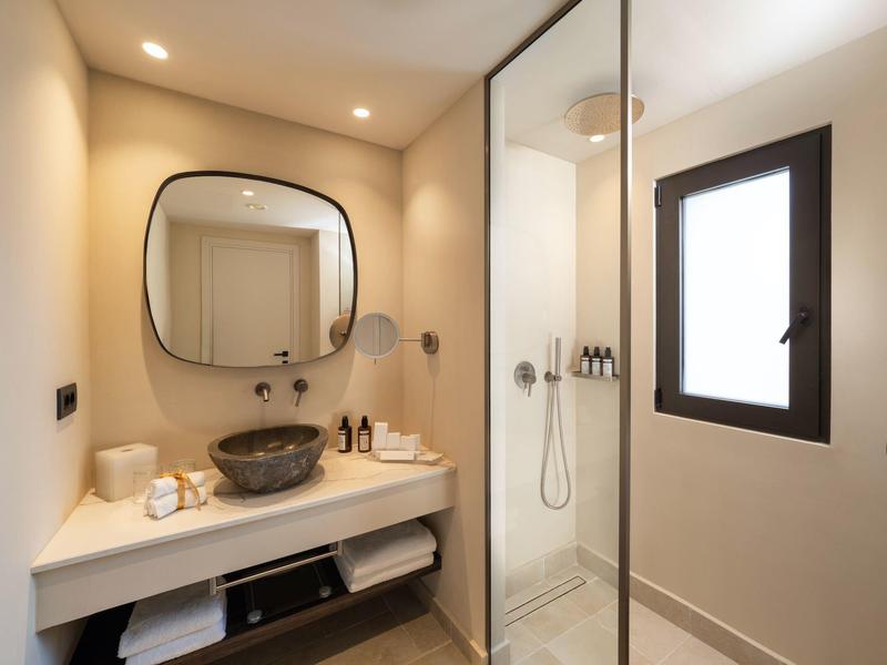 Moderner Badezimmerspiegel über weißem Waschtisch mit grauer Schale, Glastür und Fenster.