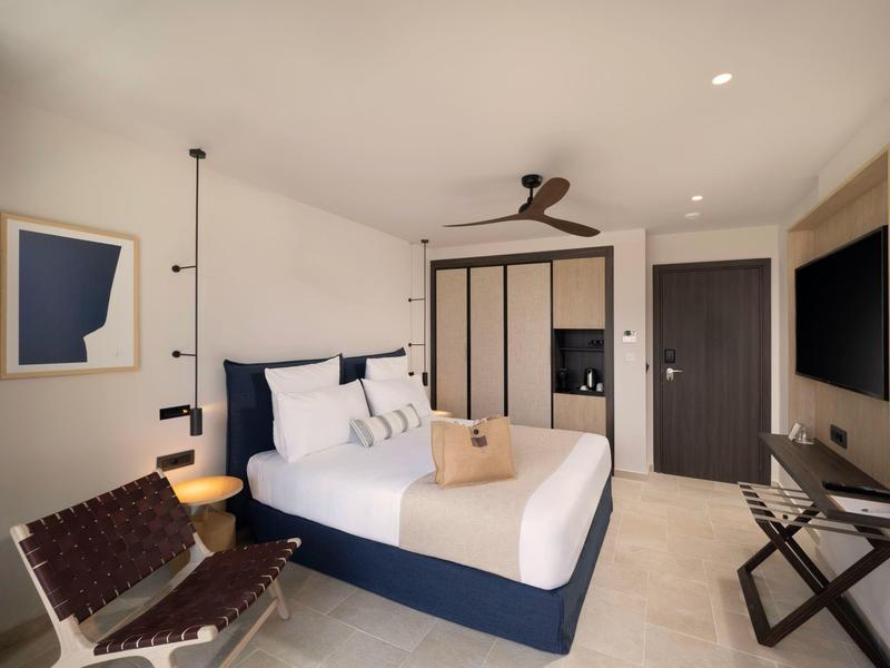 Modernes Schlafzimmer mit Doppelbett, braunem Stuhl, Deckenventilator und weißen Wänden.