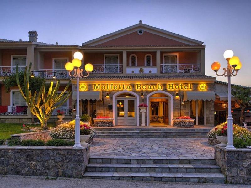 Ingang van een verlicht hotel met lantaarns en verzorgde voortuin in de schemering.